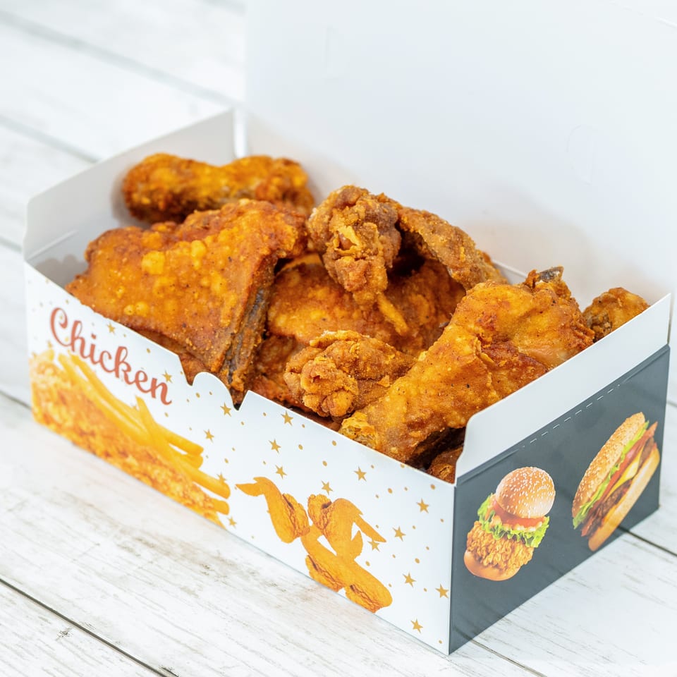 Box of crispy fried chicken pieces in branded packaging on a white wooden table.