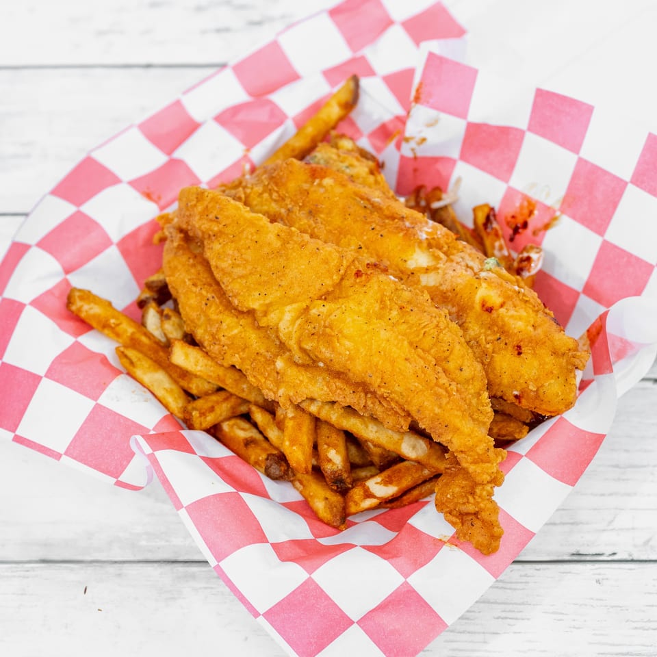 Crispy fried fish fillets and golden fries served in a red-and-white checkered basket liner.