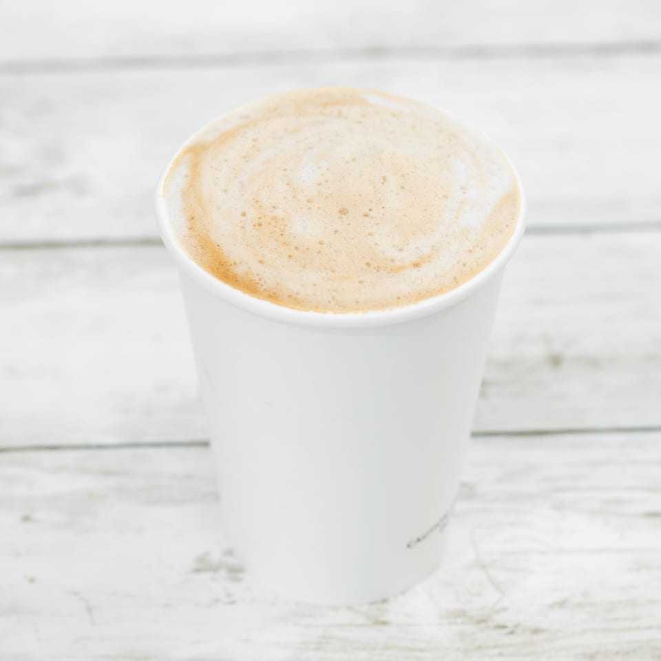 Foamy latte in a white cup on a rustic white wooden table.