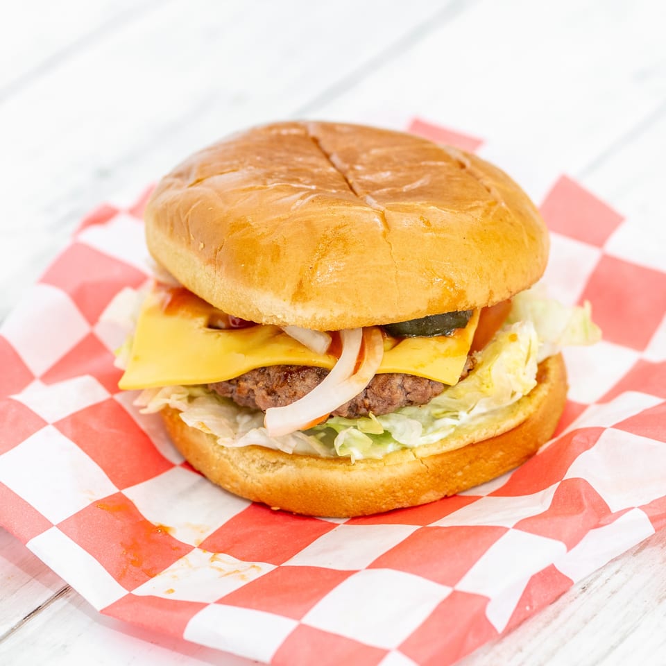 Double cheeseburger with lettuce, onions, pickles, and tomato on a toasted bun, served on red-and-white checkered paper.