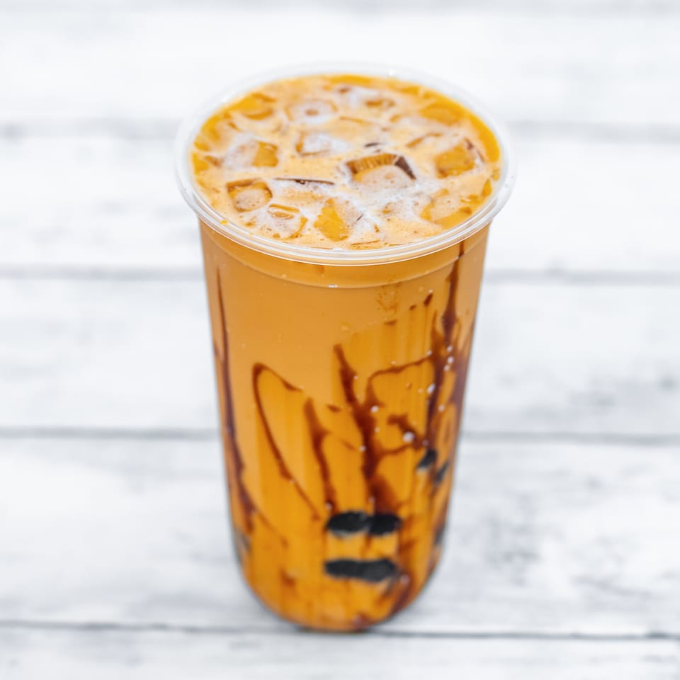 Iced caramel coffee in a clear plastic cup topped with foam and drizzled with chocolate sauce.